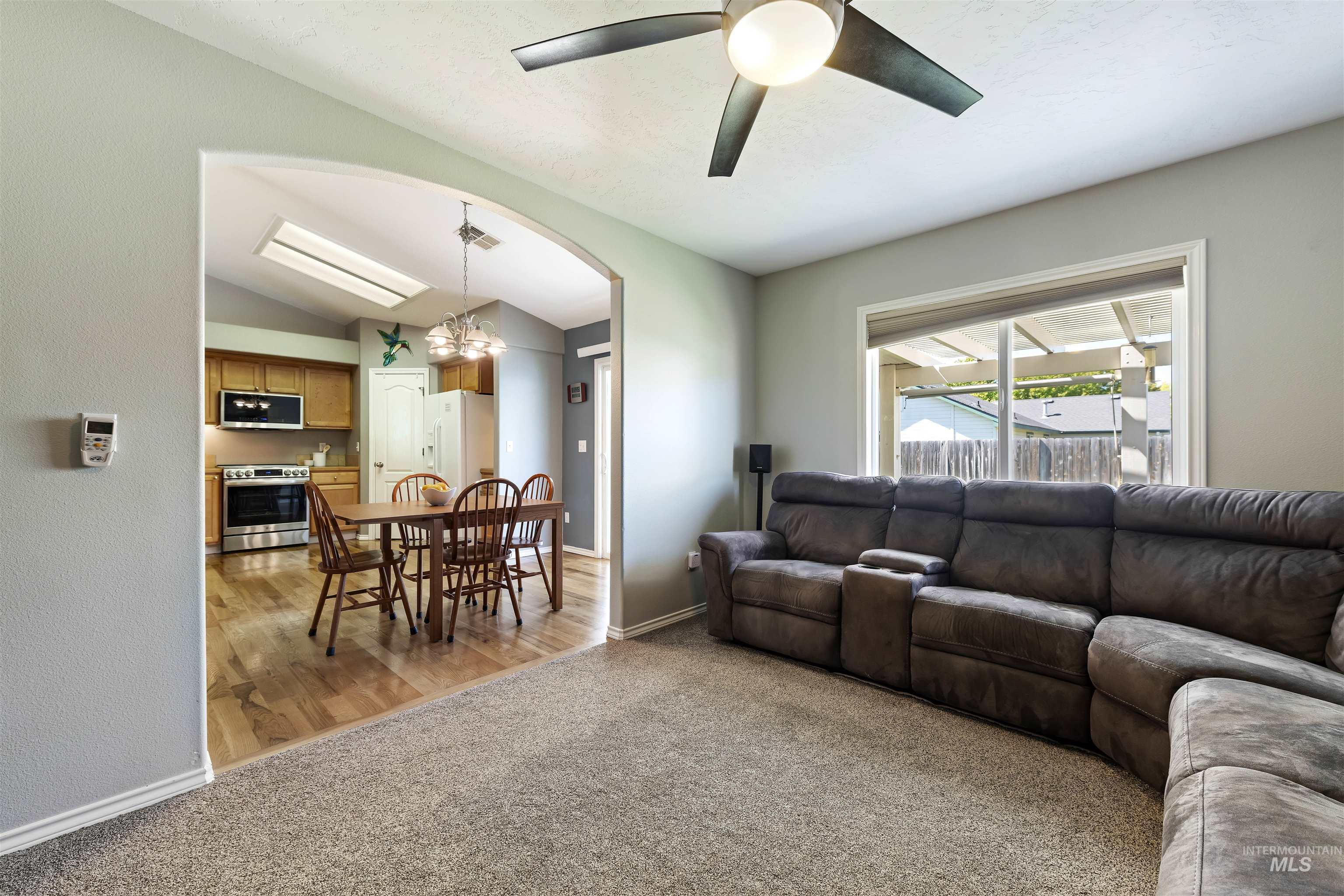 2175 North CapeCod Way Meridian, ID 83646 - Photo 7 of 23 Carpeted living area with a ceiling fan and a large window, featuring an arched doorway opening to a kitchen with wood-finish flooring, wood cabinetry, and stainless steel appliances