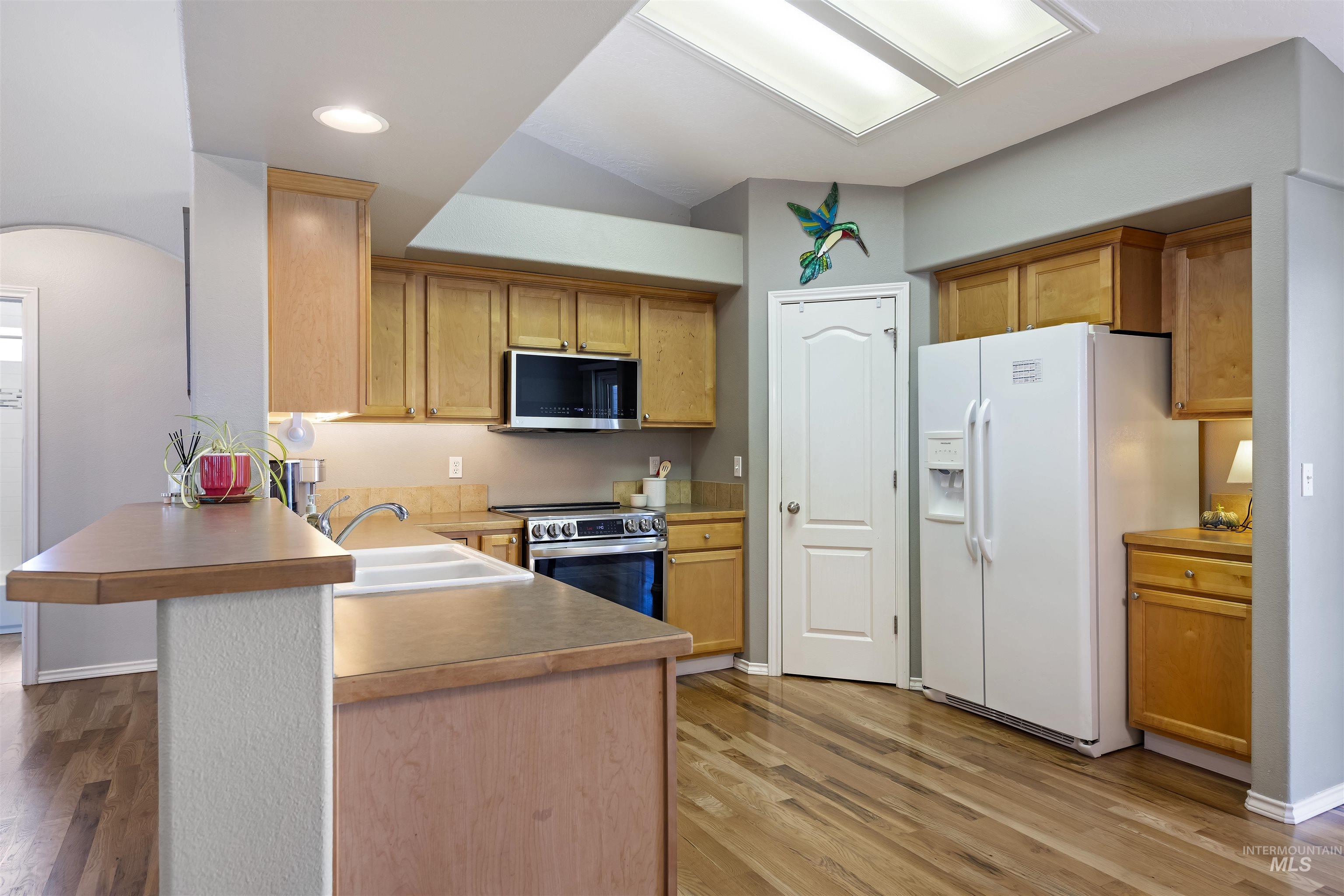 2175 North CapeCod Way Meridian, ID 83646 - Photo 9 of 23 Kitchen featuring wood-finish flooring, light wood cabinetry, white double basin sink, stainless steel oven with microwave, and an integrated breakfast bar