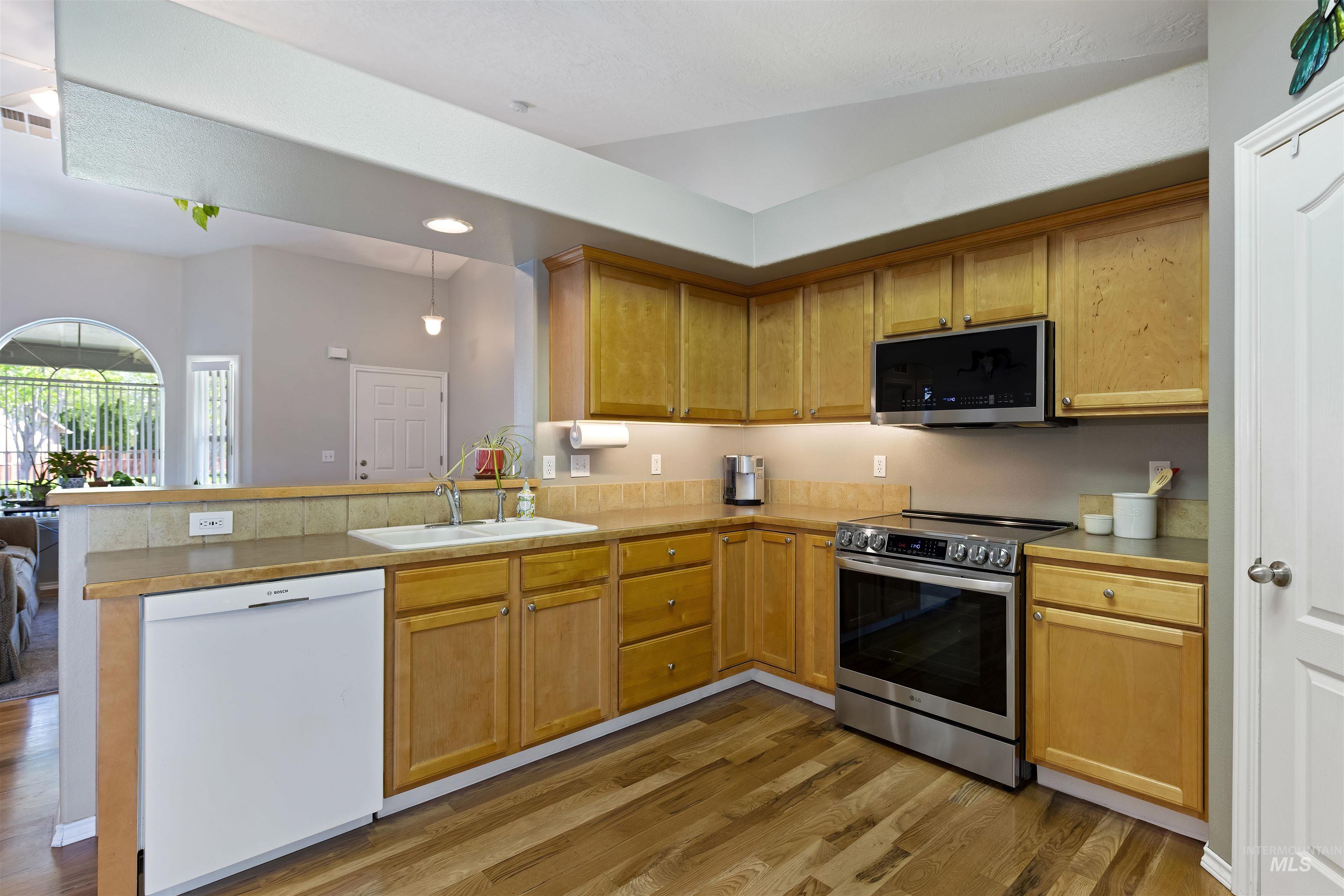 2175 North CapeCod Way Meridian, ID 83646 - Photo 10 of 23 Contemporary kitchen featuring wood-finish flooring, light wood cabinetry, stone countertops, a tile backsplash, and stainless steel appliances