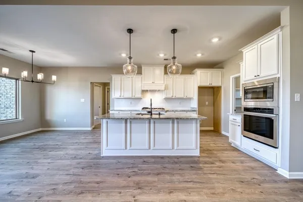 a large kitchen with stainless steel appliances kitchen island granite countertop a stove a sink a refrigerator and a wooden floor