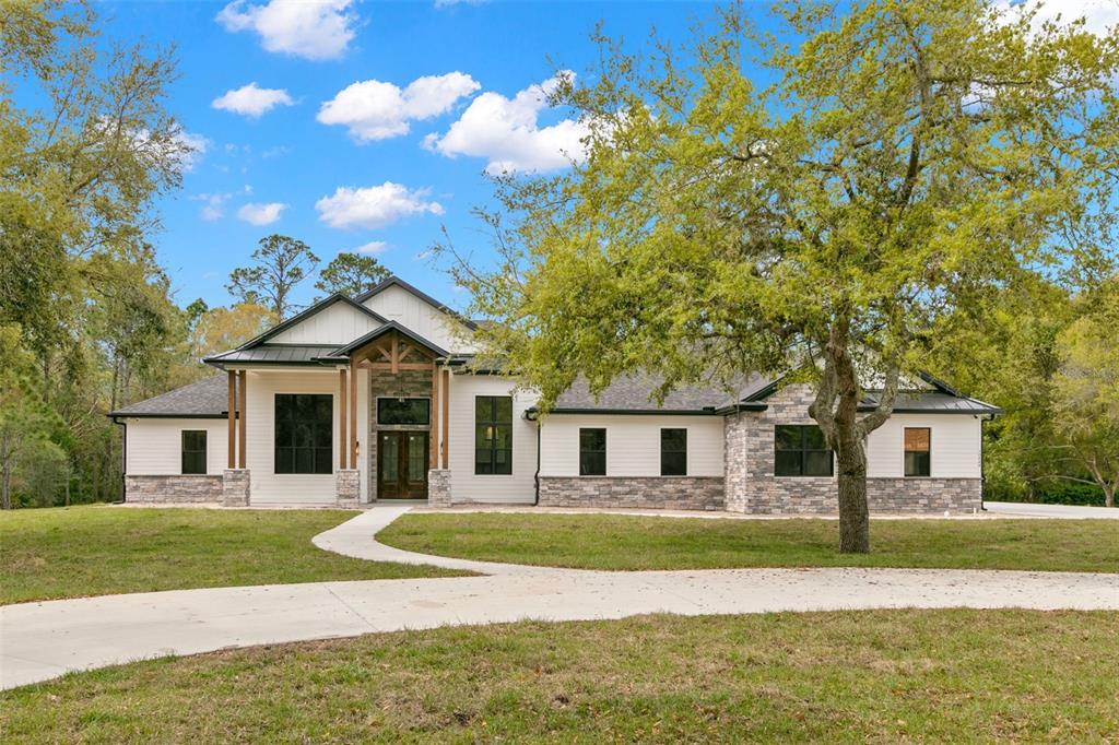 a view of a white house next to a yard with big trees