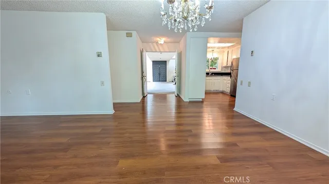 a view of an empty room with wooden floor and a kitchen