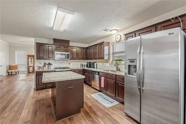 a kitchen with stainless steel appliances granite countertop a refrigerator a sink dishwasher a stove with wooden cabinets and floor