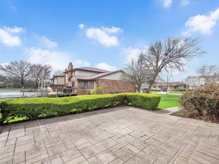 a view of a white house in front of a big yard with plants and large trees
