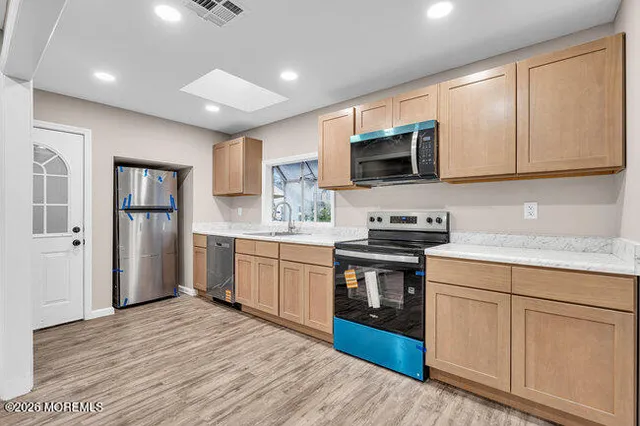 a kitchen with granite countertop a stove top oven a sink dishwasher a refrigerator and white cabinets with wooden floor