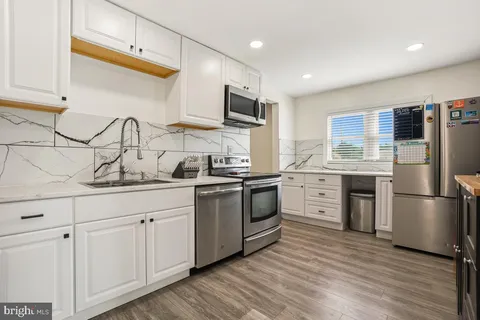 a kitchen with stainless steel appliances granite countertop white cabinets a sink a stove a refrigerator and island with wooden floor