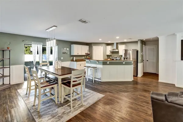 a kitchen with stainless steel appliances kitchen island granite countertop a refrigerator a stove a sink a dining table and chairs with wooden floor