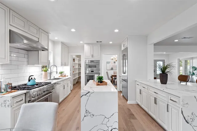a dining room with kitchen island stainless steel appliances furniture a large window and a kitchen view