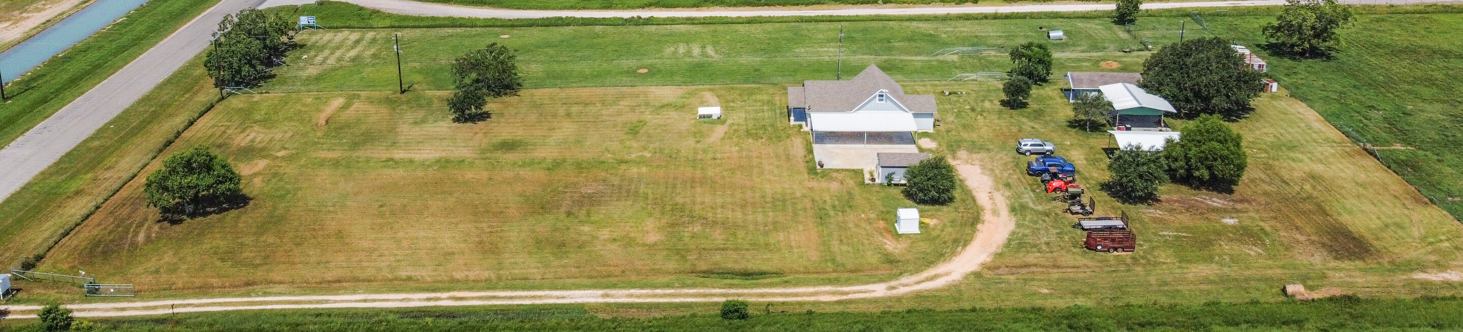 11301 South FM 441 Road El Campo, TX 77437 - Photo 7 of 43 Aerial view of part of the spacious 10 acre rural property. It features a large, open field with a few trees, a house, guest house, and several outbuildings. The property is accessible by paved FM road.