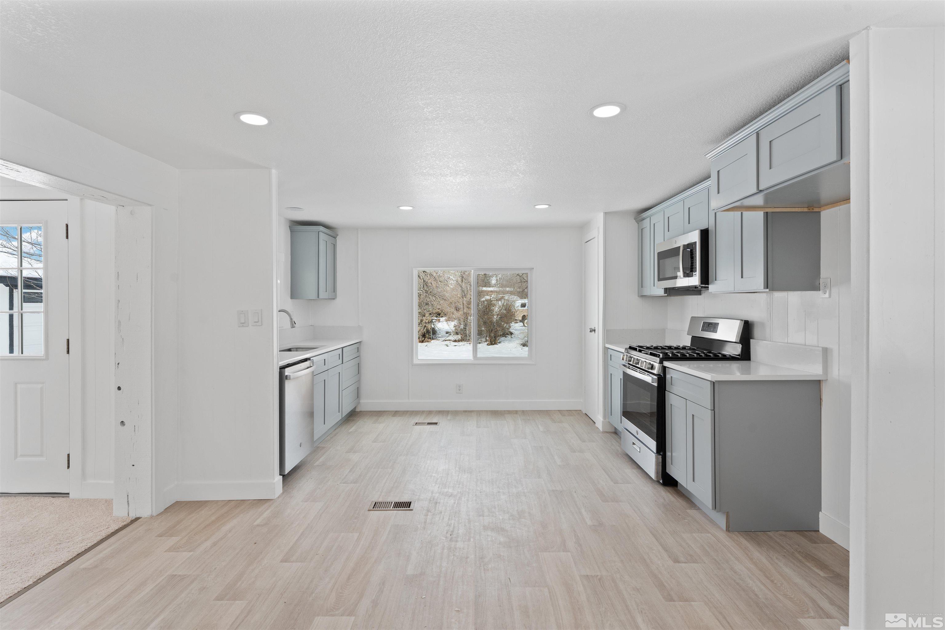 3993 Kiwi Court Reno, NV 89508 - Photo 6 of 39 a large white kitchen with granite countertop a stove a sink a refrigerator and white cabinets with wooden floor