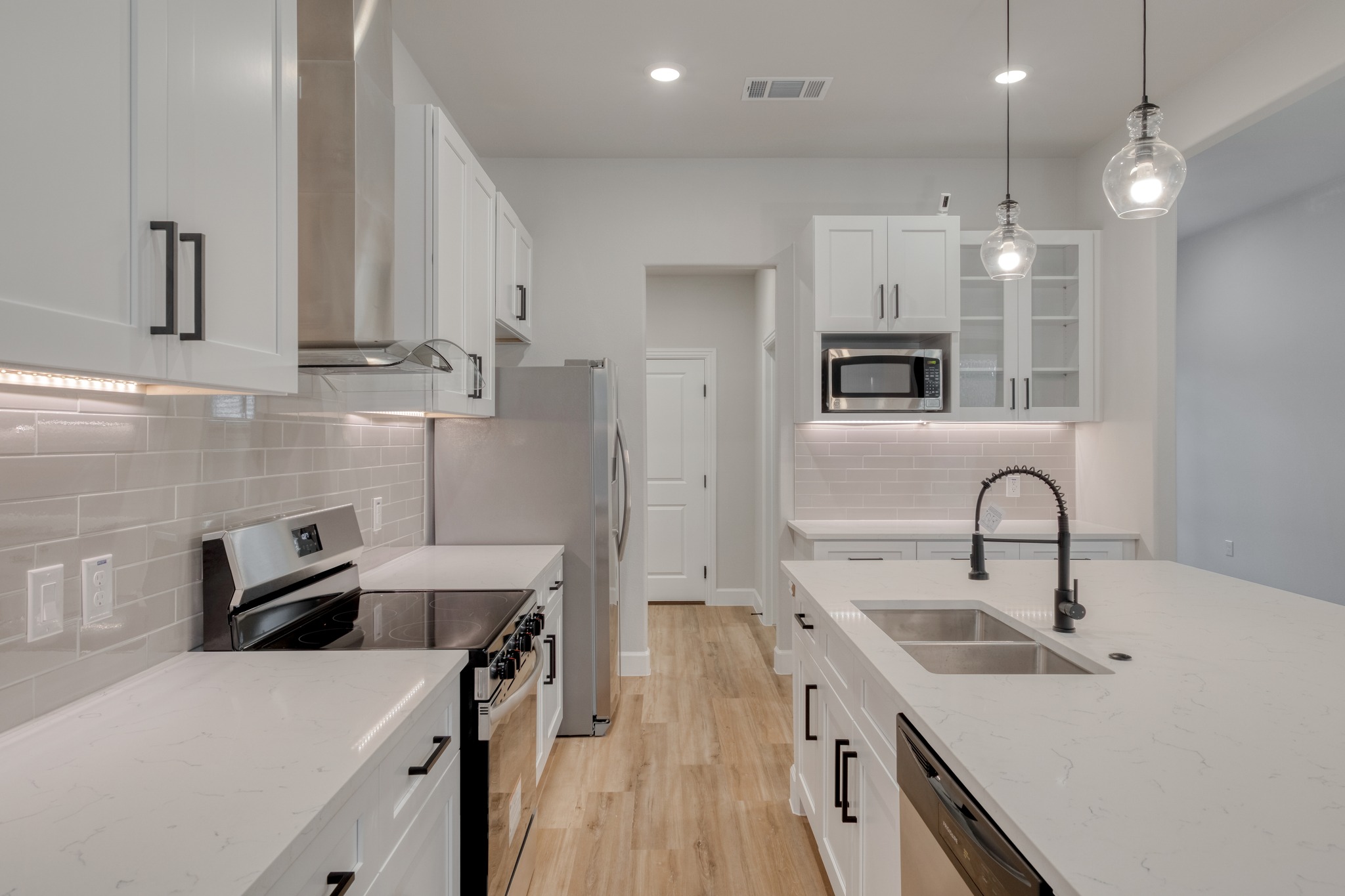 116 Pine Point Cove Elgin, TX 78621 - Photo 11 of 27 Bright kitchen featuring white cabinetry with matte black hardware, stainless steel appliances, light wood-finish flooring, and a large island with an undermount double sink