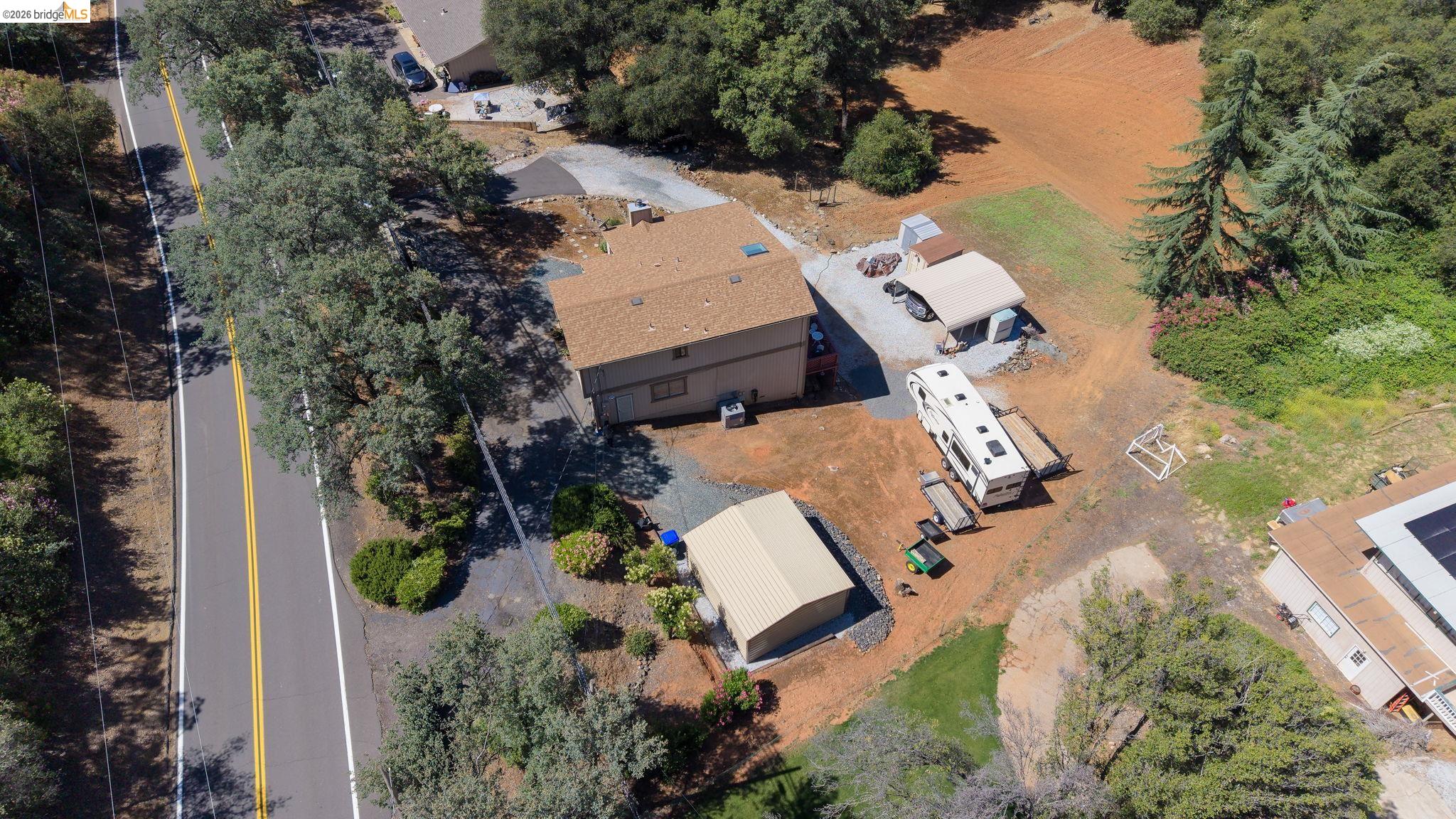 11858 Campo Seco Road Sonora, CA 95370 - Photo 45 of 45 Property with a two-story residence featuring a brown shingle roof, a detached metal-sided storage building, a separate covered parking structure, a paved road frontage, and mature trees lining the property