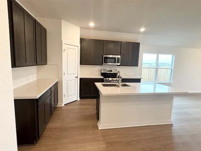 a kitchen with stainless steel appliances a stove top oven a sink a refrigerator white cabinets and wooden floor