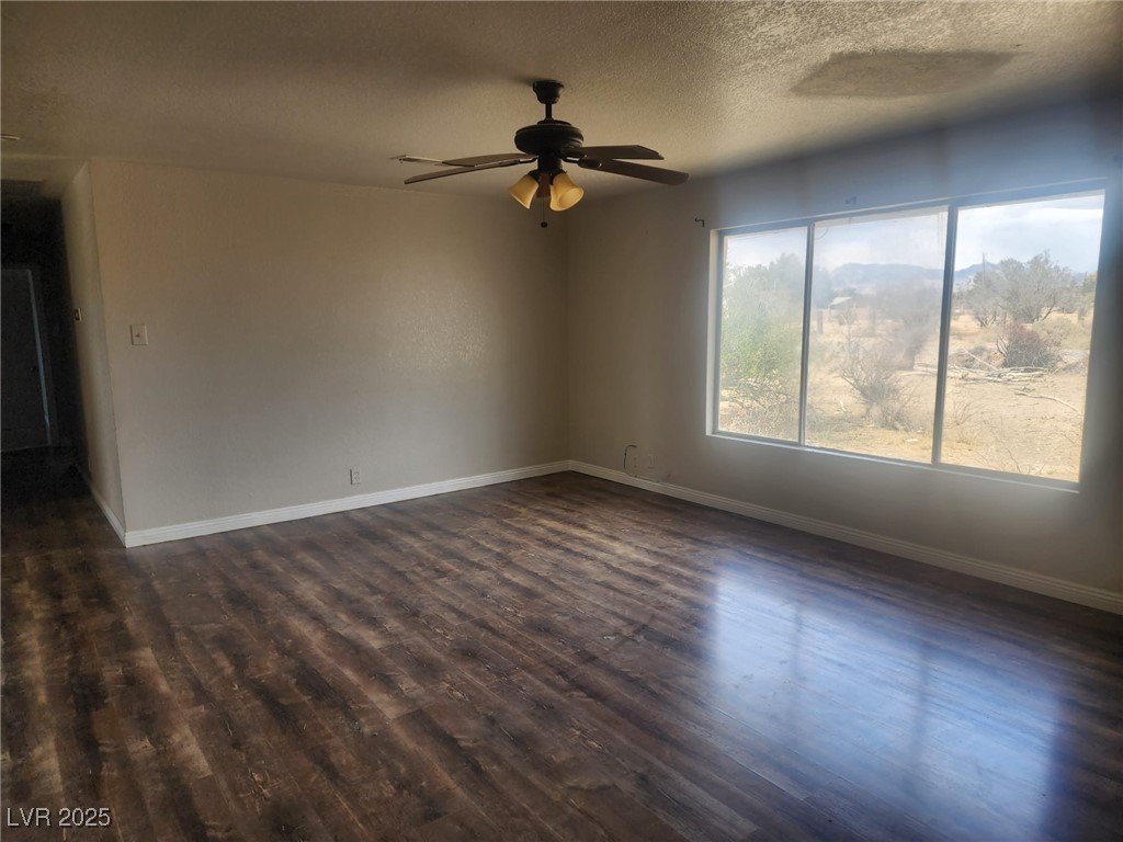 781 Buol Road Pahrump, NV 89048 - Photo 8 of 13 Empty room featuring dark wood finished floors, a ceiling fan, baseboards, and a textured ceiling
