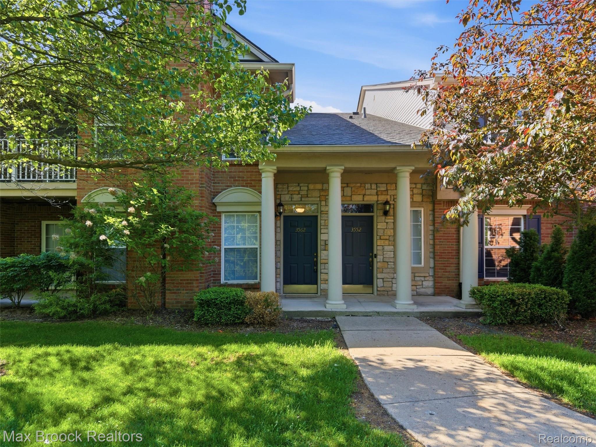 3562 Tremonte Circle Rochester, MI 48306 - Photo 1 of 33 Brick and stone facade townhome featuring a covered entry with columns, dark paneled doors, and mature landscaping