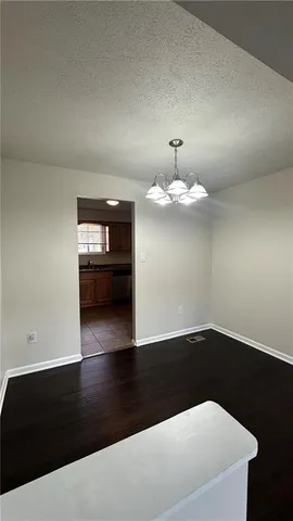 a view of an empty room with wooden floor and a kitchen