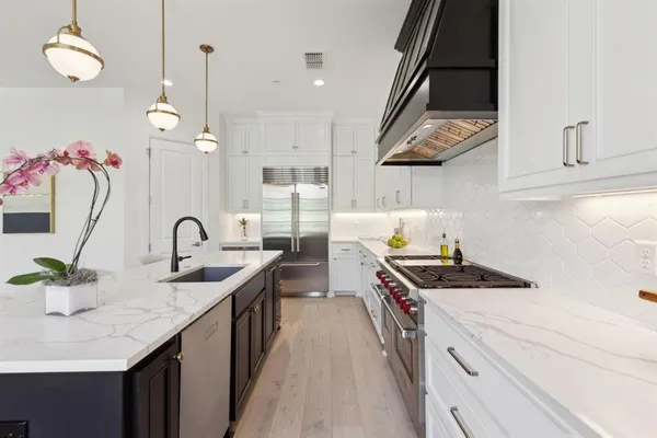 a kitchen with a stove a kitchen island a sink dishwasher a dining table and chairs with wooden floor