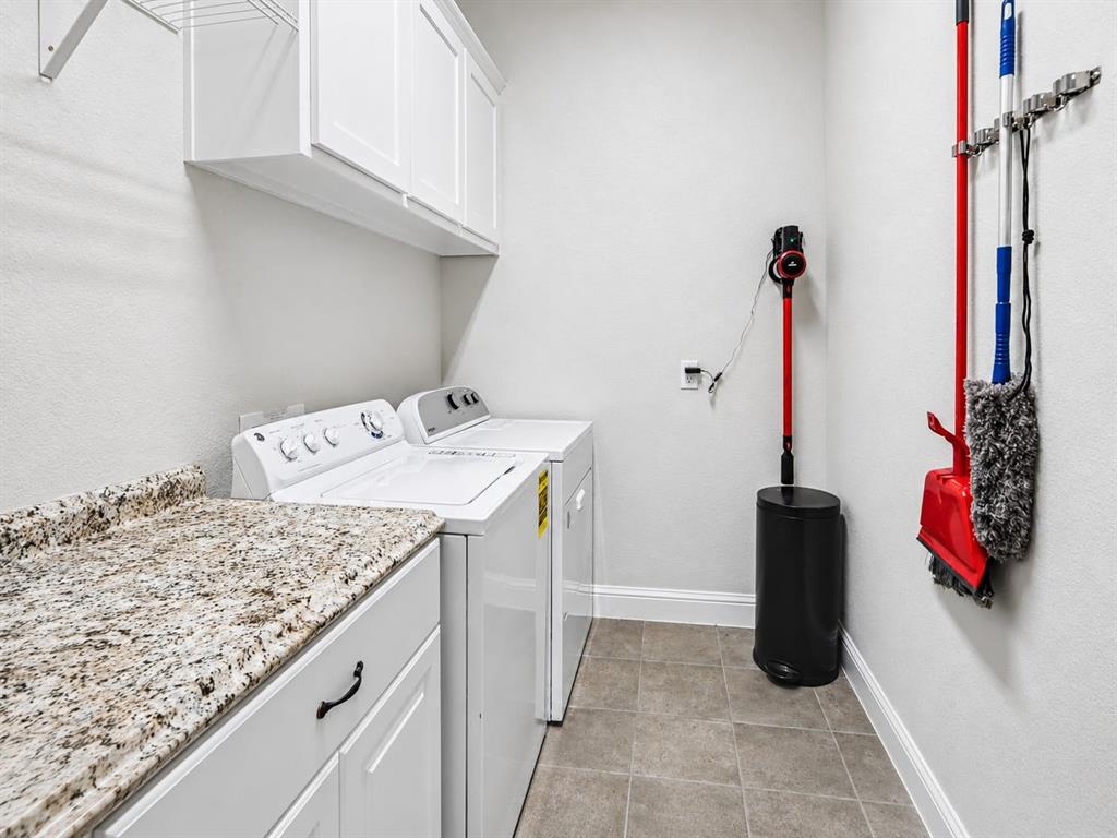 5213 Ravine Ridge Court Flower Mound, TX 76262 - Photo 26 of 40 Dedicated laundry area featuring a granite-style countertop, white cabinetry with dark hardware, and neutral tile flooring, and extra cabinet space.