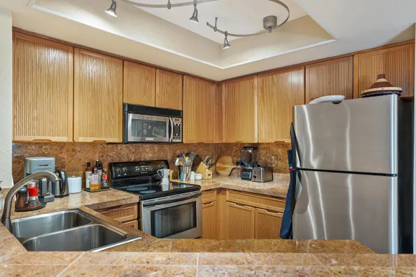 a kitchen with stainless steel appliances granite countertop a refrigerator a sink dishwasher a stove with wooden cabinets and floor