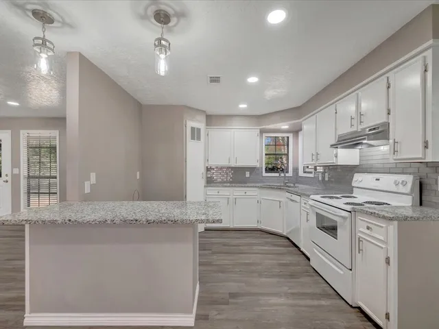 a large white kitchen with granite countertop a stove top oven a sink a counter space and cabinets