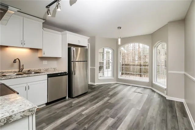 a kitchen with granite countertop a refrigerator a sink and white cabinets