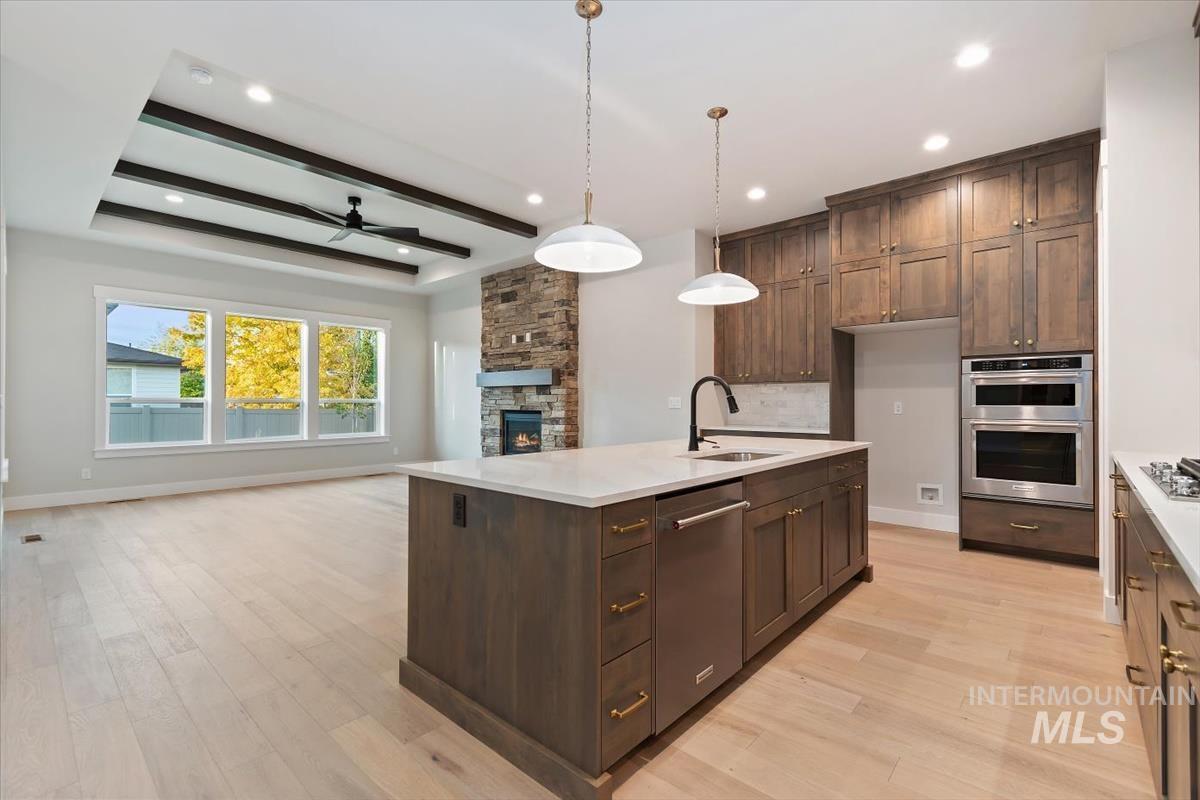 2147 East Blakehurst Avenue Kuna, ID 83634 - Photo 43 of 43 Kitchen featuring beam ceiling, a stone fireplace, decorative light fixtures, open floor plan, and light wood-style flooring