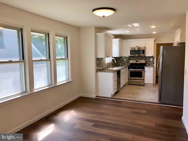 a kitchen with stainless steel appliances granite countertop a stove a refrigerator and a sink with wooden floors