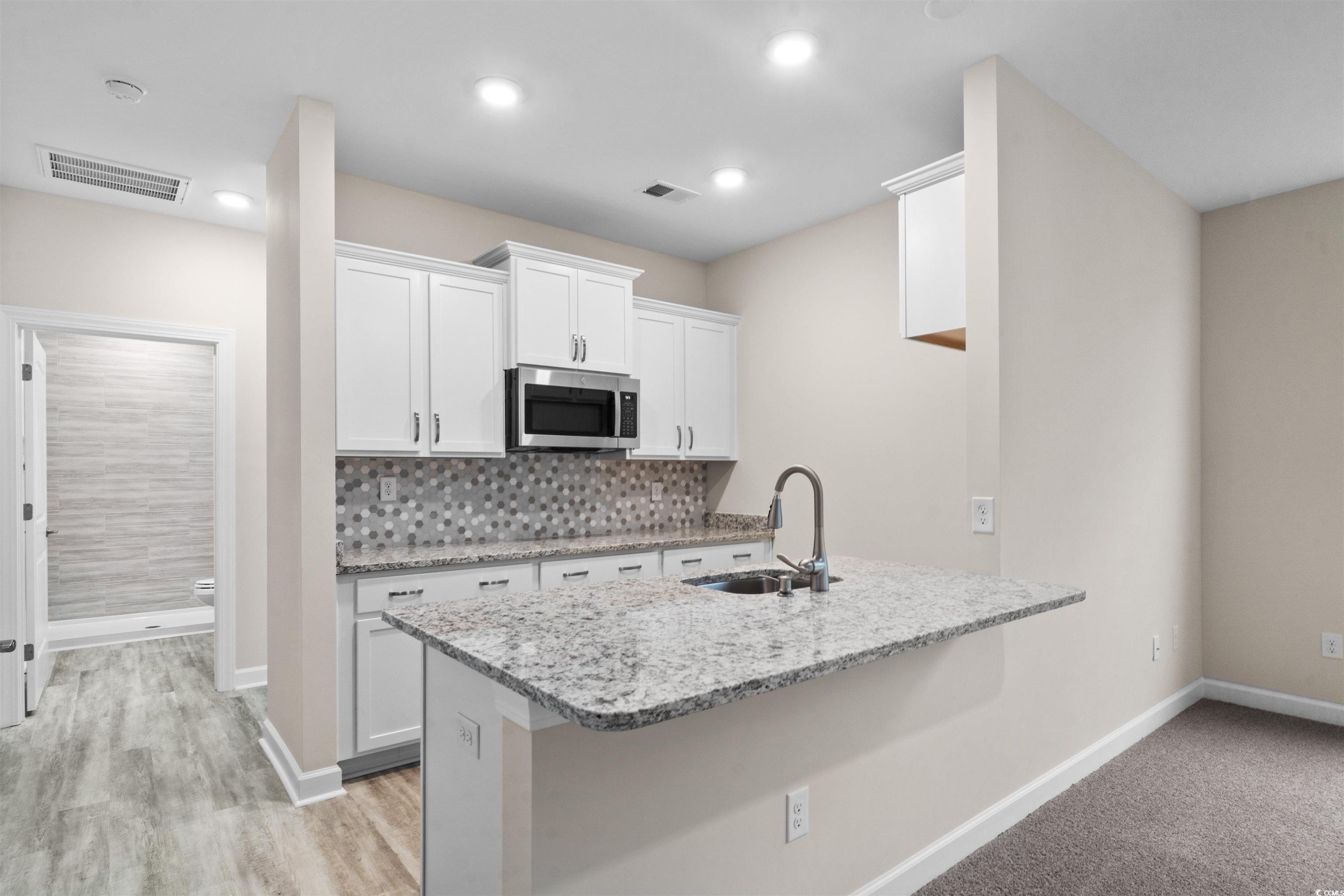1906 Woodrush Loop Little River, SC 29566 - Photo 7 of 40 Kitchen featuring white cabinets, light stone counters, sink, and light colored carpet