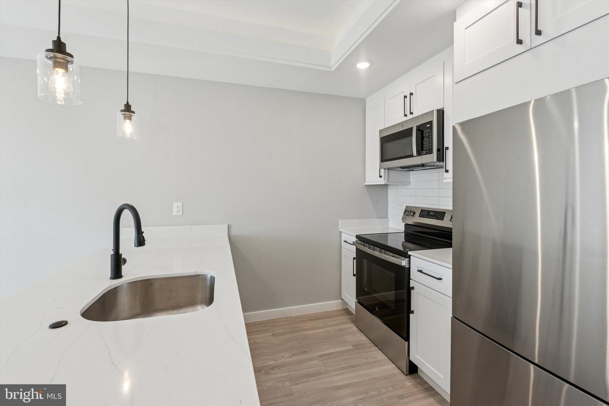 a kitchen with stainless steel appliances a sink a stove a refrigerator with white cabinets