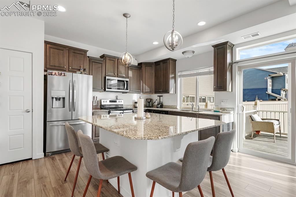 9319 Timberlake Loop Colorado Springs, CO 80927 - Photo 8 of 25 a kitchen with stainless steel appliances granite countertop a refrigerator a stove a sink a dining table and chairs with wooden floor