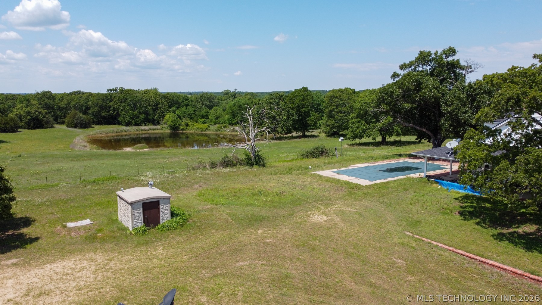 13248 North 3540th Road Maud, OK 74854 - Photo 11 of 98 Expansive acreage featuring a private pond, a covered outdoor pool, mature trees, a stone utility building, and a distant residential structure