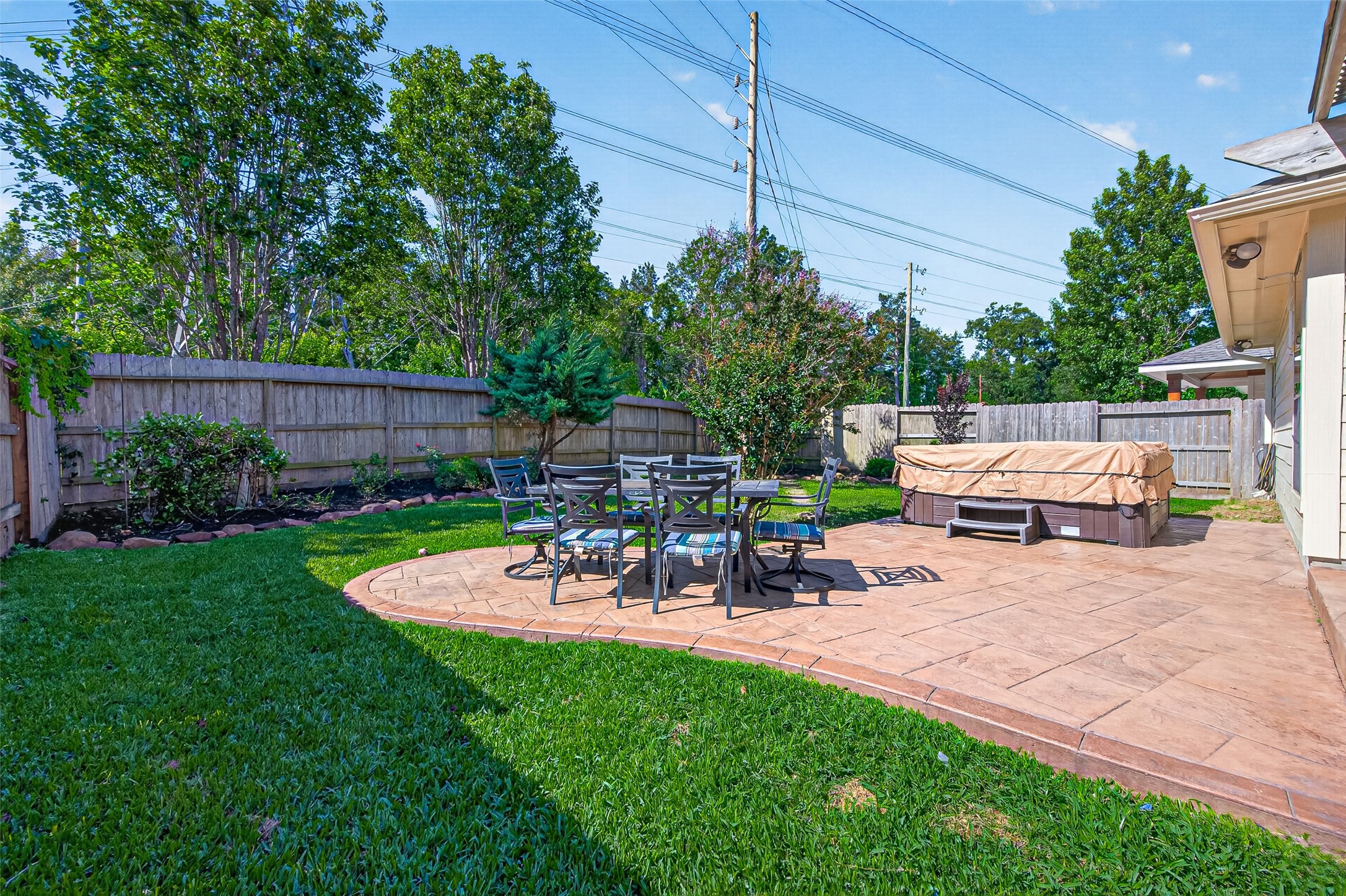 27443 Rebecca Field Lane Spring, TX 77386 - Photo 29 of 31 This backyard features a spacious patio with a dining set and a covered hot tub, surrounded by lush greenery and privacy fencing, perfect for outdoor relaxation and entertaining.