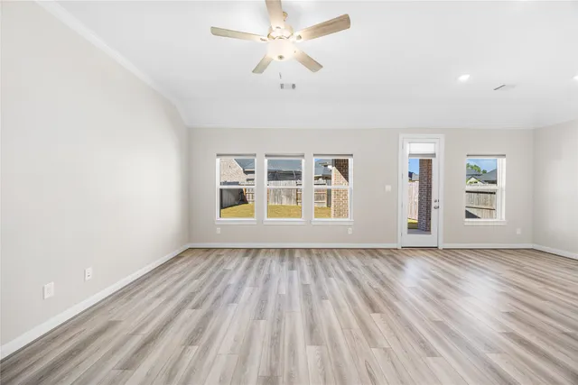 an empty room with wooden floor chandelier fan and windows