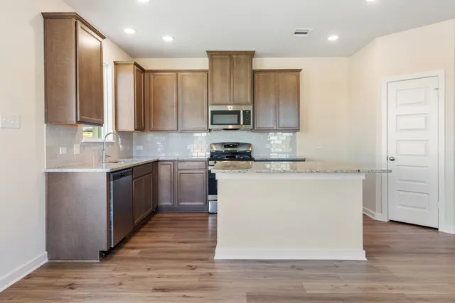 a kitchen with kitchen island granite countertop wooden floors white cabinets and stainless steel appliances