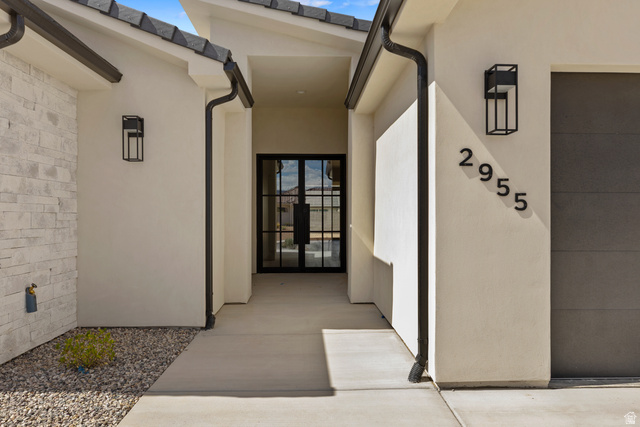 2955 East Rimrunner Drive St. George, UT 84790 - Photo 6 of 35 Entryway featuring a modern double-door with black framing, stucco exterior, stacked stone accent wall, decorative exterior lighting, and a paved walkway