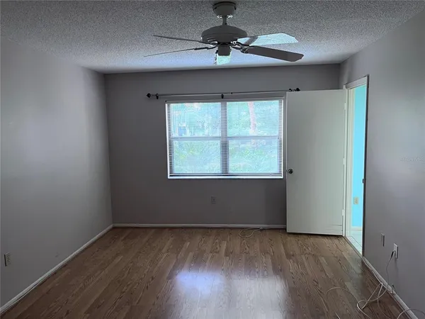 an empty room with wooden floor chandelier fan and windows