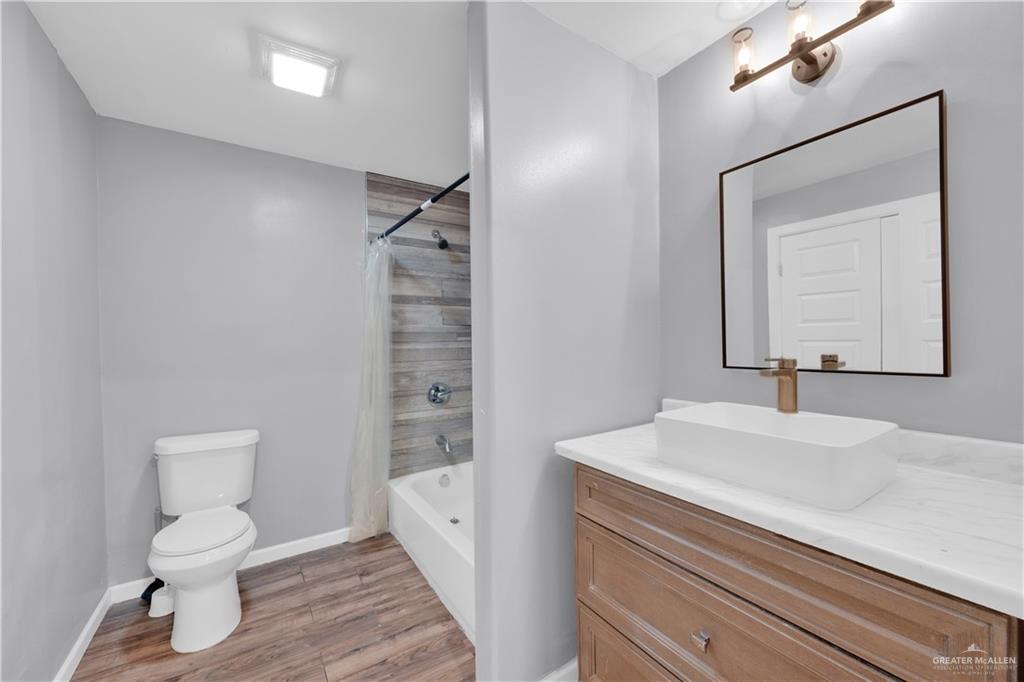 405 East Guerra Street Rio Grande City, TX 78582 - Photo 8 of 33 Bathroom with vanity, toilet, wood finished floors, shower / tub combo with curtain, and baseboards