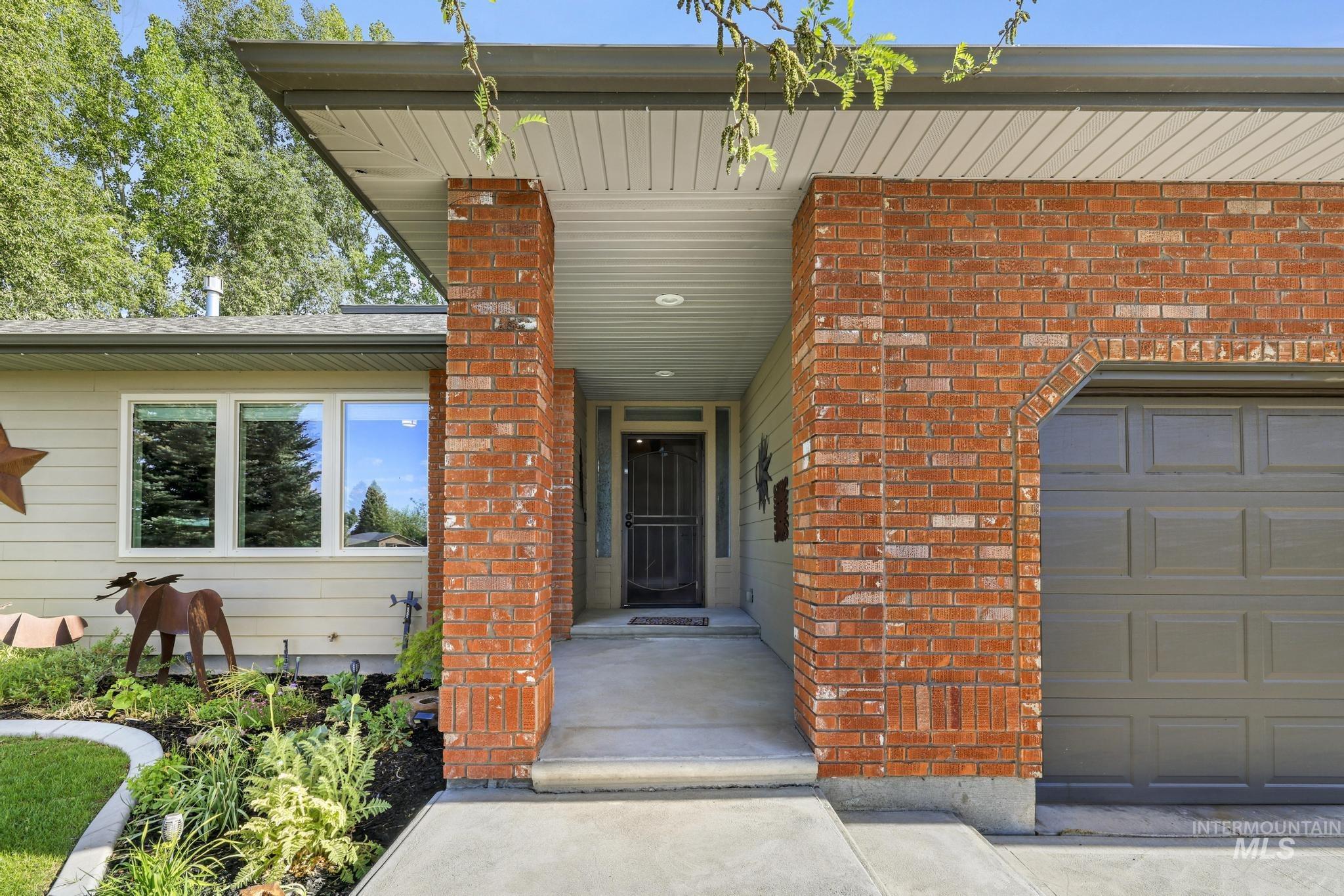 Brick facade with an integrated single-car garage, concrete walkway, and landscaped front garden