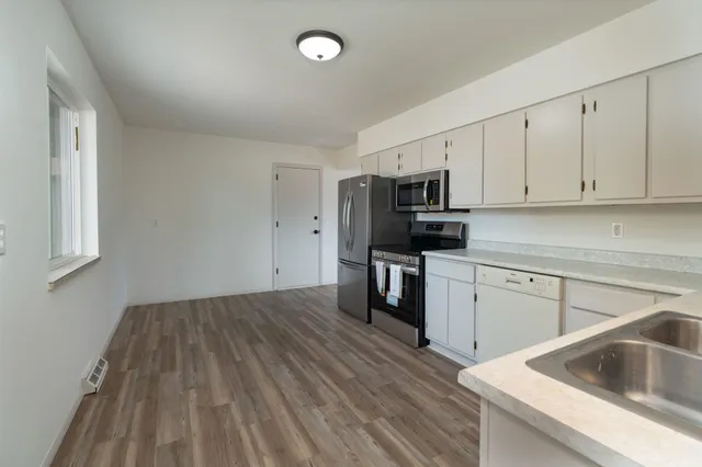 a kitchen with granite countertop a sink dishwasher stove and white cabinets with wooden floor