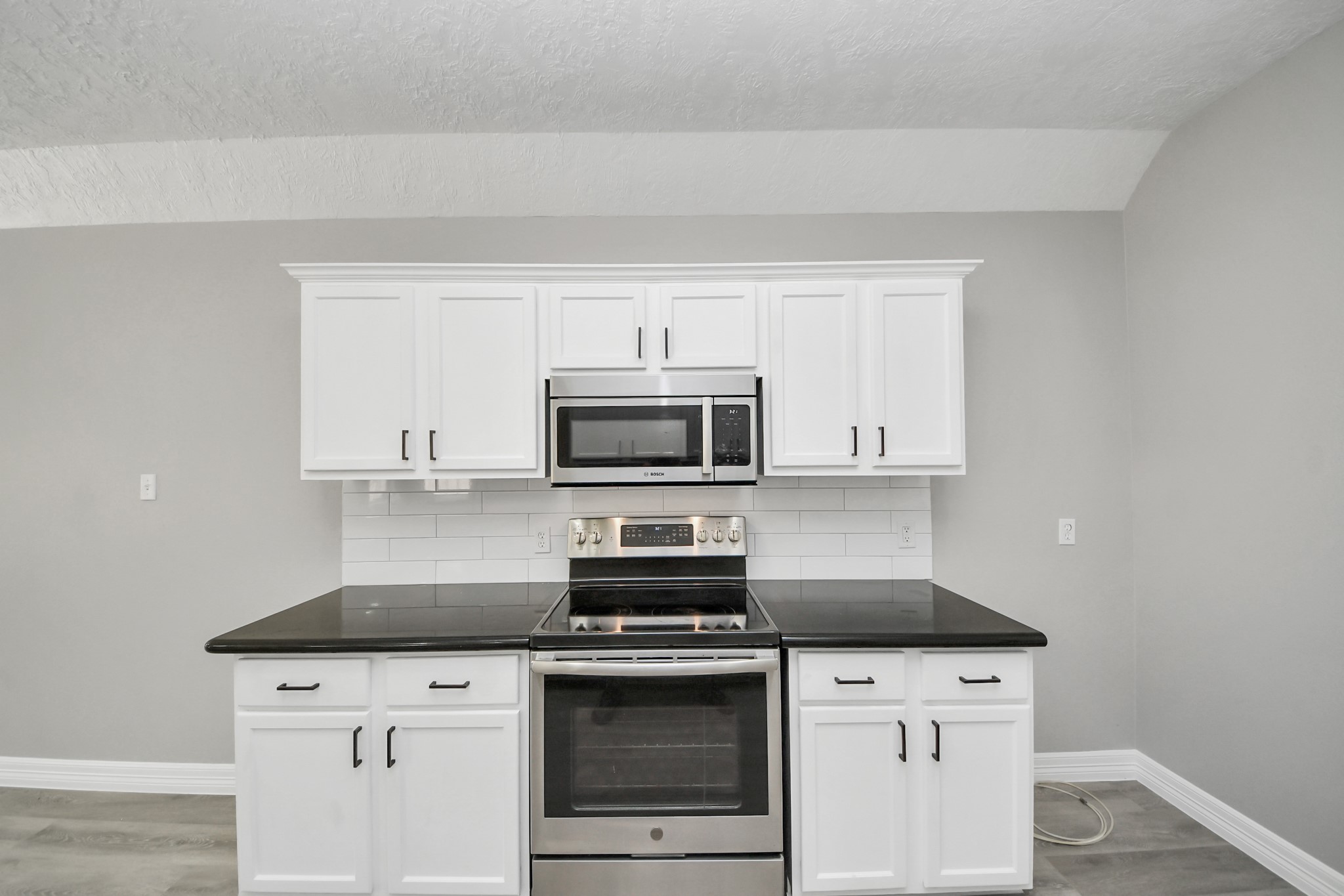 1105 East Kyle Road Clute, TX 77531 - Photo 12 of 44 The modern kitchen with sleek black countertops, white cabinetry, and stainless steel appliances, including a stove and microwave.