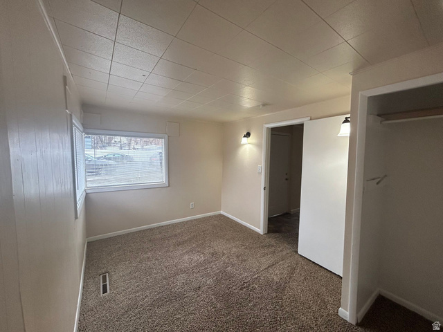 265 Rigdon Avenue, Unit 1 Salt Lake City, UT 84115 - Photo 10 of 15 Carpeted interior room featuring a window with blinds, a closet opening with a hanging rod, wall-mounted light fixtures, and a ceiling with square paneling