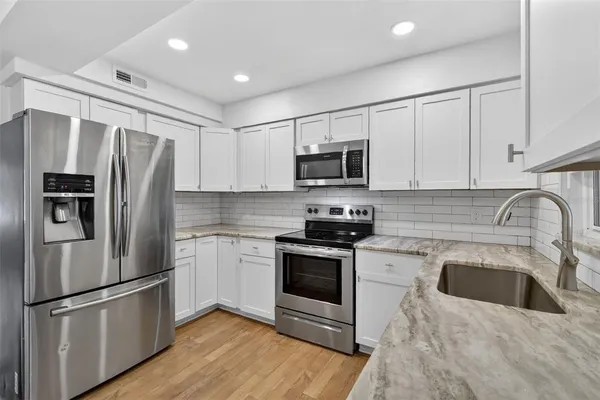 a kitchen with stainless steel appliances granite countertop a refrigerator stove a sink and white cabinets