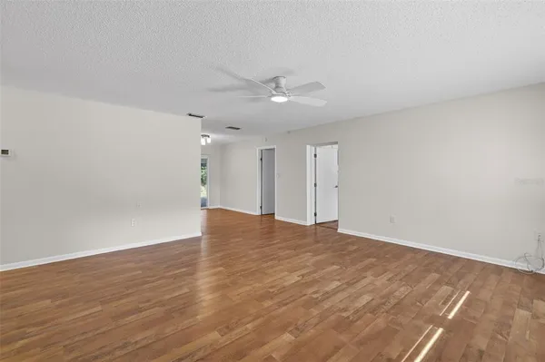 a view of an empty room with wooden floor and a ceiling fan