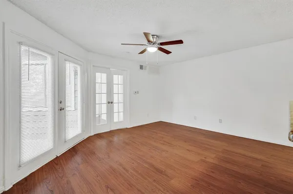 an empty room with wooden floor fan and windows