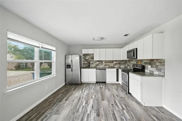 a kitchen with stainless steel appliances a refrigerator a sink dishwasher stove and white cabinets with wooden floor