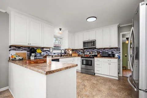 a kitchen with stainless steel appliances granite countertop a stove top oven a sink a refrigerator and white cabinets