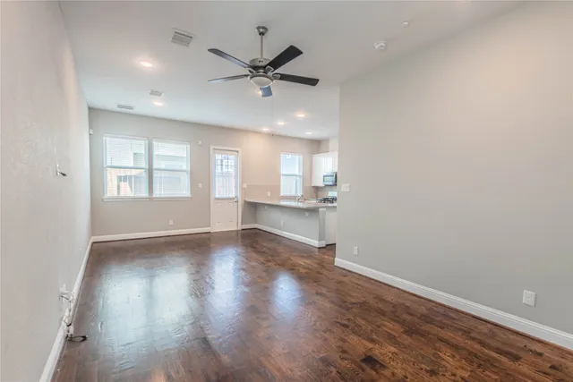 an empty room with wooden floor fan and windows