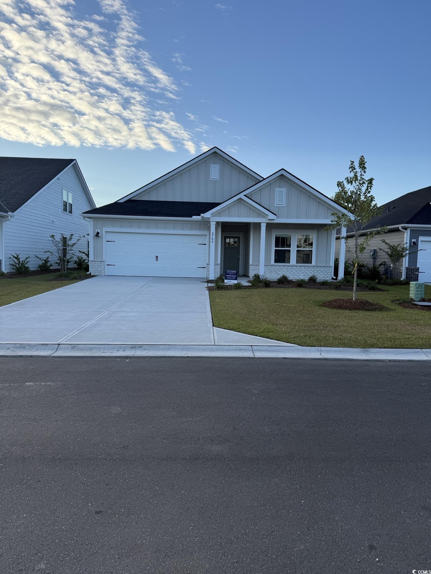 View of front of house with a front yard, board and batten siding, driveway, and a garage