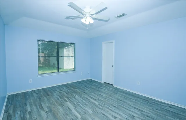 an empty room with wooden floor chandelier fan and windows