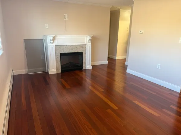 a view of an empty room with wooden floor and a fireplace